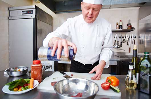 A chef drizzling oil into a silver bowl while preparing